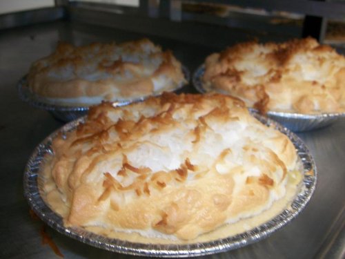 Three golden-brown coconut cream pies with fluffy meringue topping in silver pie tins.
