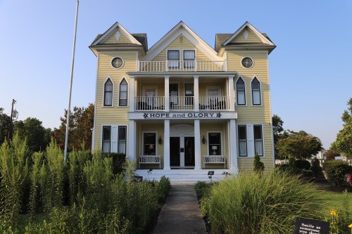 A yellow Victorian-style house with balconies, labeled "Hope and Glory," surrounded by greenery and a clear blue sky.