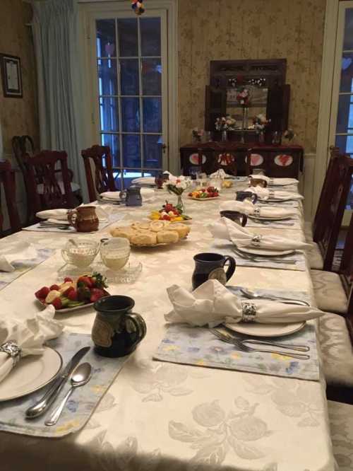 A beautifully set dining table with elegant tableware, flowers, and a variety of dishes, ready for a gathering.