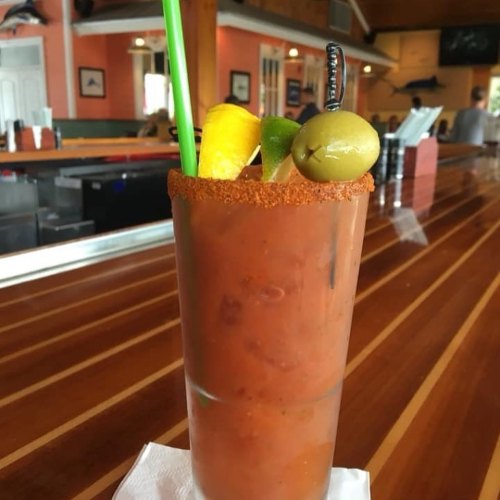 A vibrant Bloody Mary garnished with lime, lemon, and an olive, served in a glass on a wooden bar counter.