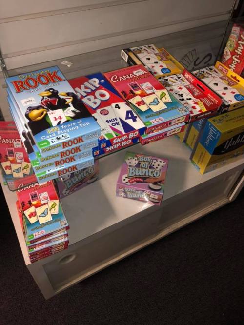 A display of various board games and card games, including Rook, Skip-Bo, and Bunco, stacked on a table.