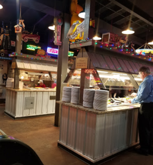 A rustic restaurant interior with buffet stations, colorful lights, and a man serving food at one of the counters.