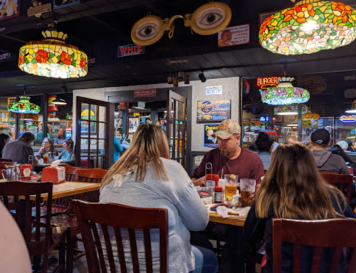 A busy restaurant interior with stained glass lamps, patrons dining at tables, and a lively atmosphere.