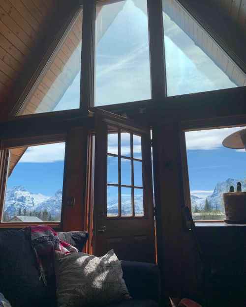 Cozy interior with large windows showcasing a snowy mountain landscape and bright blue sky.