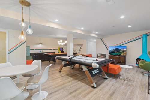 A modern game room featuring an air hockey table, dining area, TV, and colorful wall accents.