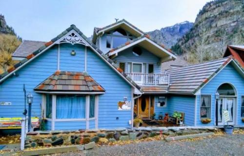 A charming blue house with a unique roof design, surrounded by mountains and featuring a stone pathway.