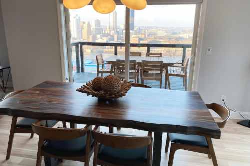 A wooden dining table with chairs, featuring a decorative centerpiece, overlooking a city skyline through large windows.