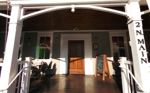 A wooden entrance with a large door and a chalkboard sign, framed by white columns and a porch.