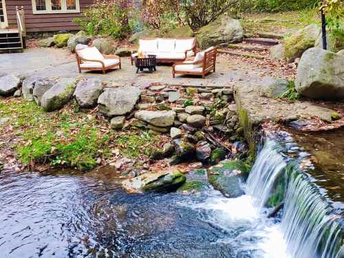 A cozy outdoor seating area by a small waterfall, surrounded by rocks and greenery.