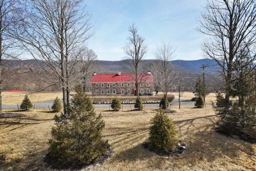 A scenic view of a building with a red roof surrounded by trees and mountains in the background on a clear day.