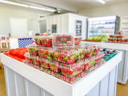 A display of stacked strawberry containers in a bright market, with fresh produce visible in the background.