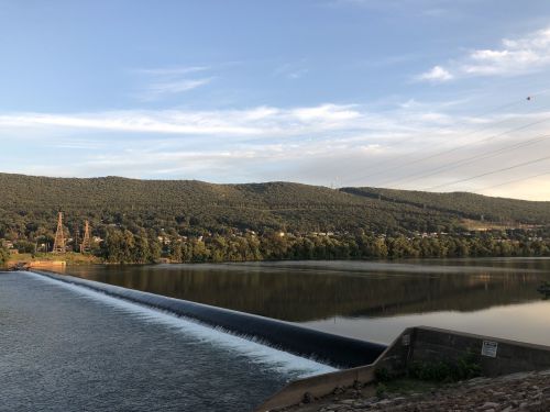 A serene landscape featuring a dam, flowing water, and lush green hills under a clear sky.