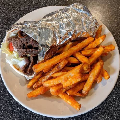 A plate with a wrapped sandwich filled with beef and vegetables, accompanied by a side of crispy sweet potato fries.