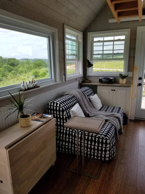 Cozy interior of a tiny home featuring a patterned sofa, side table, and large windows with a scenic view.