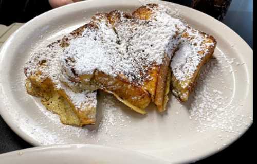 A plate of French toast dusted with powdered sugar, served warm and golden brown.