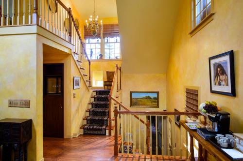 A warm, inviting foyer with a staircase, chandelier, and artwork on the walls, featuring wooden accents and a coffee station.