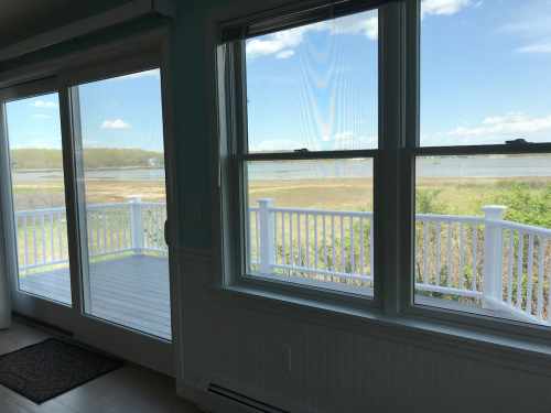 View from a room with large windows overlooking a deck and a scenic landscape with grass and water.