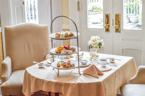 A beautifully set table with a three-tiered stand of assorted pastries and fruits, next to a cozy armchair.