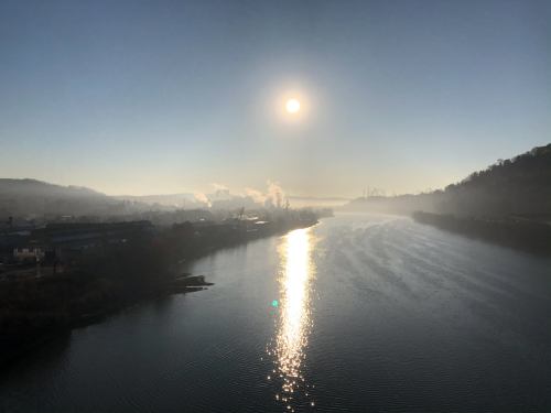 A serene river scene at sunrise, with mist rising and industrial buildings in the background.