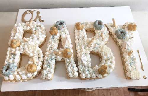 A dessert display spelling "Oh BABY!" decorated with cream, donuts, and various sweet treats on a white board.