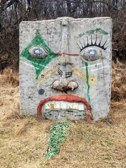 A large, colorful concrete face sculpture with exaggerated features, set against a grassy background.