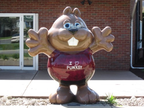 A large, cartoonish beaver statue with outstretched arms, wearing a maroon shirt that says "I ❤️ PUNXSY."