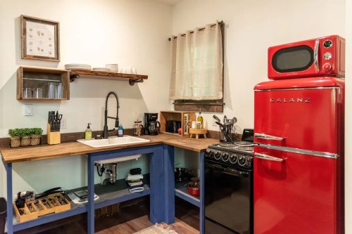 A modern kitchen featuring a red retro fridge, wooden shelves, and a sink with a stylish faucet.