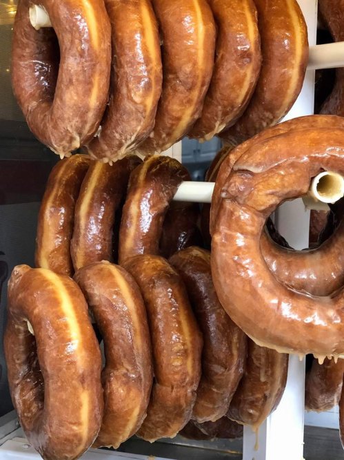 A display of freshly glazed, golden-brown donuts stacked on a rack.