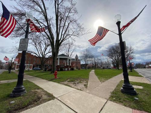 A park with American flags, lampposts, and a historic building under a cloudy sky.