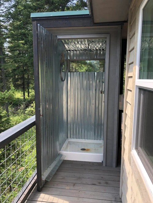 Outdoor shower with corrugated metal walls, located on a wooden deck surrounded by trees.