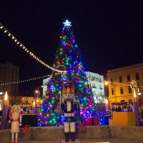 A brightly lit Christmas tree adorned with colorful lights, surrounded by festive decorations and nutcracker figures at night.