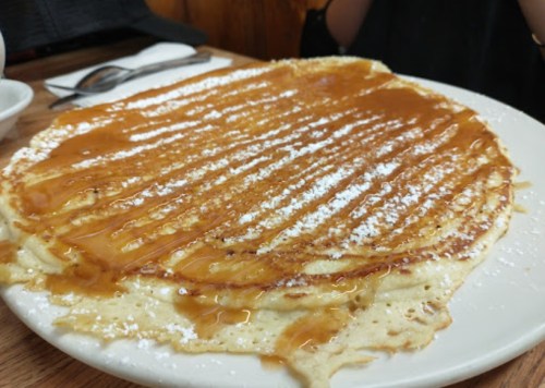 A large pancake drizzled with syrup and dusted with powdered sugar, served on a white plate.