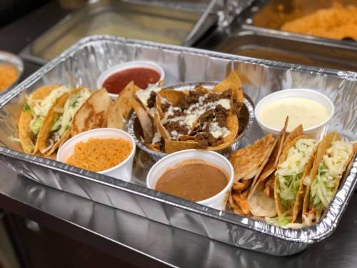 A tray of assorted tacos with sides of rice, beans, and sauces in small containers.