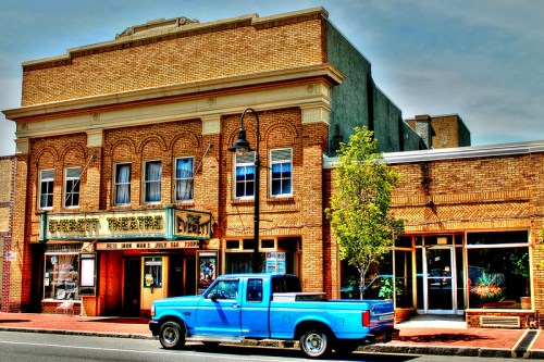 Historic theater building with a blue pickup truck parked outside, featuring ornate brickwork and a marquee.