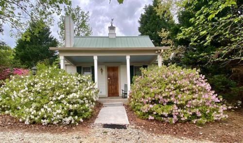 A charming cottage with a green metal roof, surrounded by blooming azaleas and a gravel pathway.