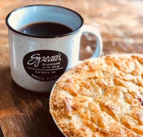 A cup of coffee next to a freshly baked pie on a wooden table, with a restaurant logo in the background.