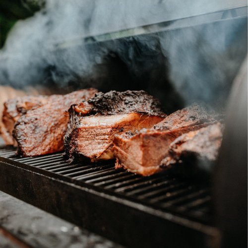 Smoky grilled meat sizzling on a barbecue, with smoke rising in the background.