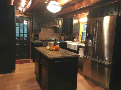 Cozy kitchen with dark cabinets, stainless steel appliances, and a central island, featuring pumpkins and a warm ambiance.