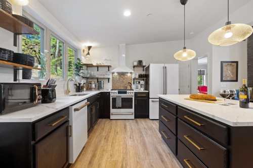 Modern kitchen with dark cabinets, white countertops, and stainless steel appliances, featuring pendant lights and a cozy atmosphere.