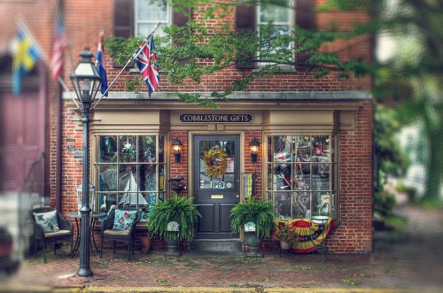 Charming gift shop with a brick facade, open sign, and potted plants, surrounded by flags and a lamppost.
