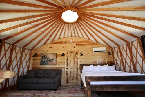Interior of a cozy yurt featuring wooden beams, a bed, a sofa, and a skylight. Warm, rustic decor.