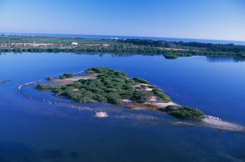 Aerial view of a lush green island surrounded by calm blue waters, with a clear sky in the background.