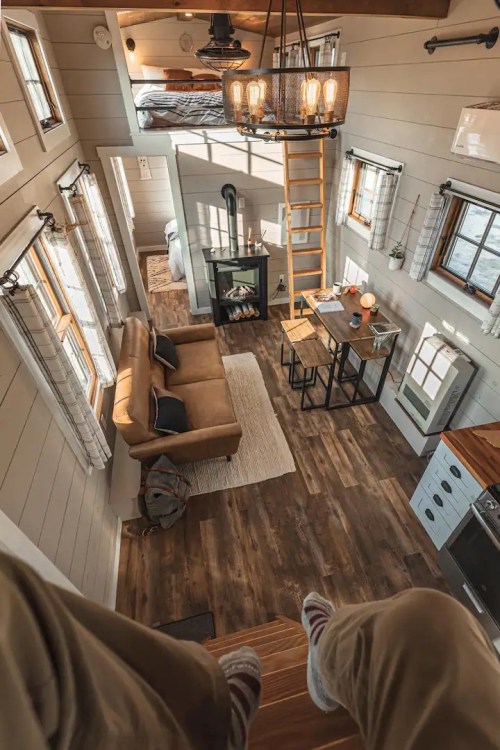 Cozy tiny home interior with a living area, kitchen, dining table, and lofted bedroom, featuring warm wood tones.