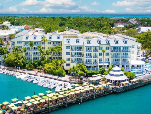 A waterfront view of a colorful hotel with boats docked and palm trees under a bright blue sky.