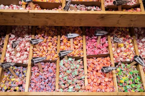 Colorful assortment of candies in wooden bins, labeled with flavors like strawberry, tangerine, and pink lemonade.