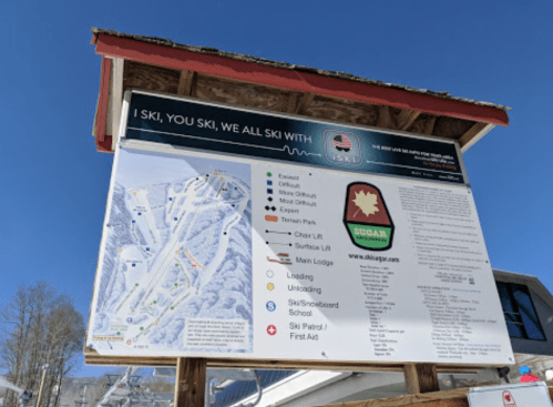 Ski resort sign displaying trail map, difficulty levels, and amenities under a clear blue sky.