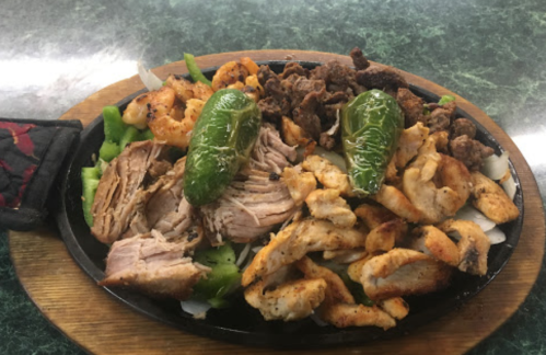 A platter of grilled meats including chicken, pork, and beef, garnished with jalapeños and served on a bed of greens.