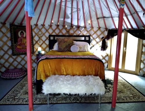 Cozy interior of a yurt featuring a bed with colorful bedding, a fluffy bench, and decorative elements.