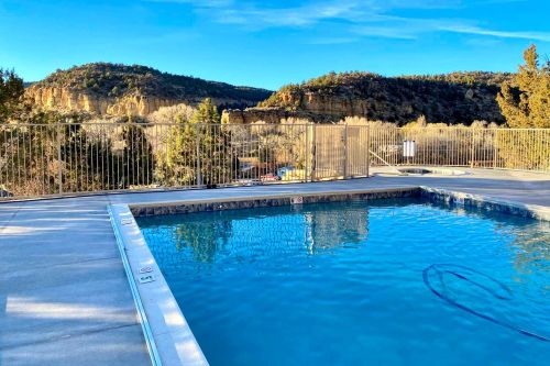 A serene pool with clear water, surrounded by trees and mountains under a blue sky.