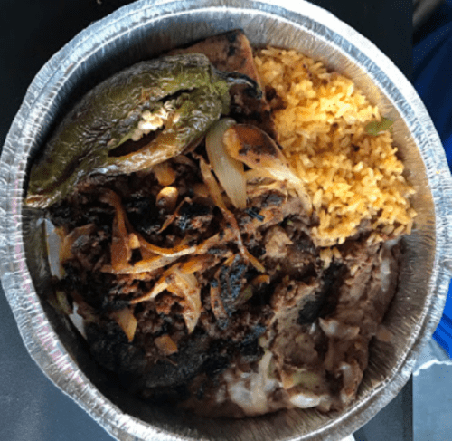 A metal takeout container filled with rice, grilled meat, onions, and a stuffed pepper.